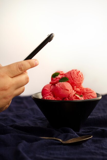 Person taking photo of ice cream scoops in bowl with smartphone