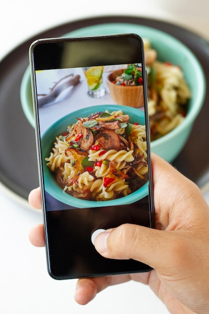 Person taking photo of pasta bowl with smartphone