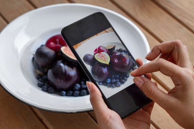 Free photo person taking photo of plate of fruit with smartphone