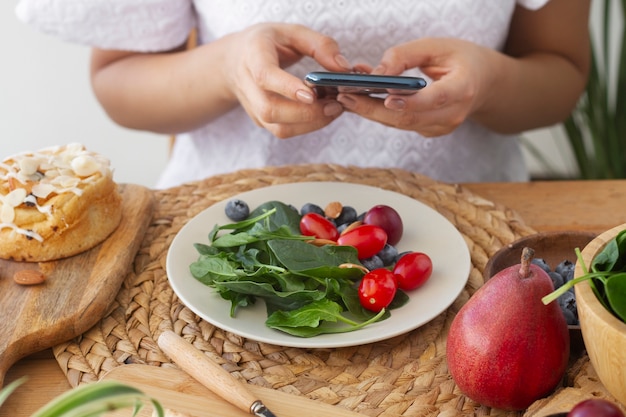 Foto gratuita persona che scatta foto di un piatto di pomodori, mirtilli e spinaci con lo smartphone