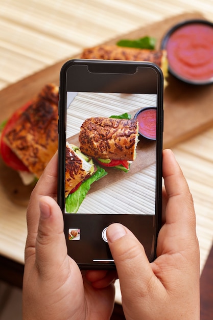 Free photo person taking photo of sandwich and ketchup with smartphone