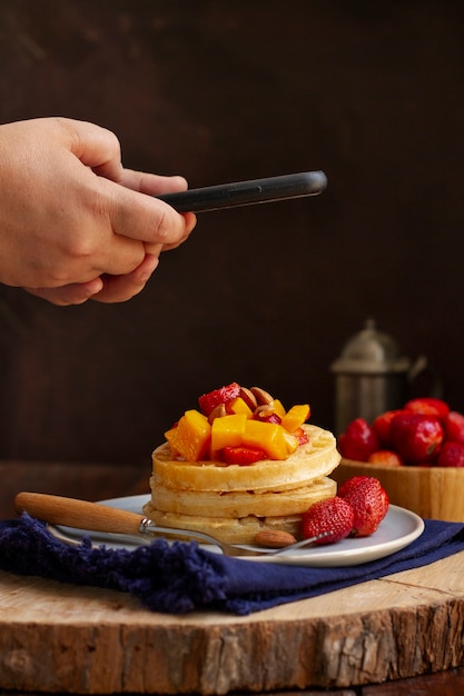 Person taking photo of waffles and strawberries with smartphone