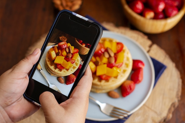 Person taking photo of waffles and strawberries with smartphone