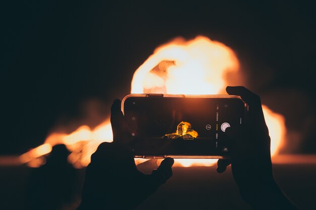 밤 시간에 스마트 폰으로 모닥불 사진을 찍는 사람