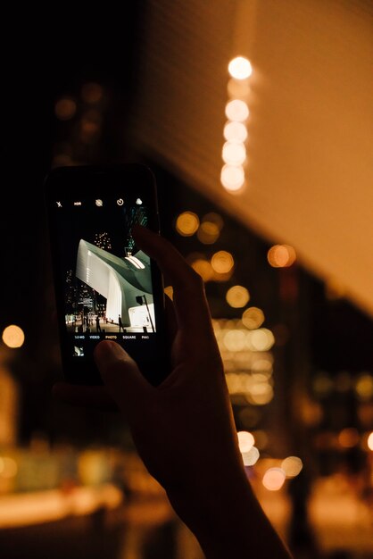 携帯電話で夜の街の近代建築の写真を撮る人