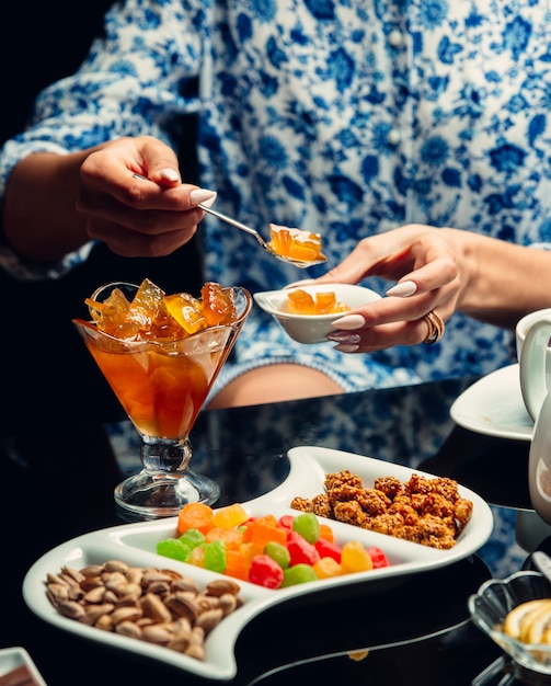 A person taking yellow confiture from tea table with sweets and nuts.