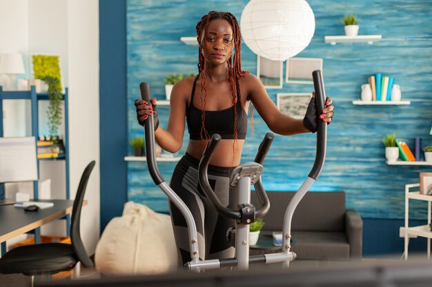 Тренировка человека в домашней гостиной на эллиптическом тренажере для кросс-кардиотренировок, просмотр упражнений онлайн