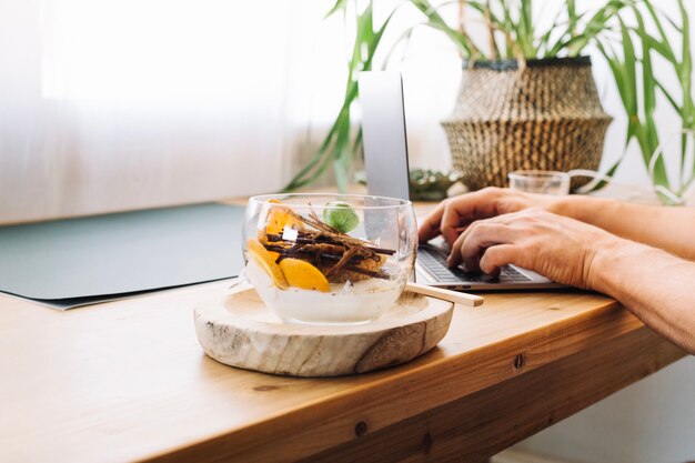 Person using laptop near bowl with dessert