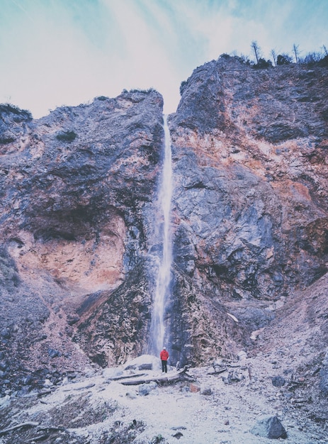Человек в красной куртке стоит возле водопадов