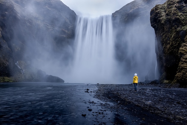 魅惑的な滝に立っている黄色いジャケットを着ている人