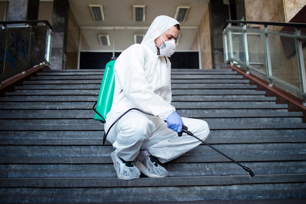 白い化学防護服を着た人が公共の廊下を消毒し、伝染性の高いコロナウイルスの拡散を阻止する手順