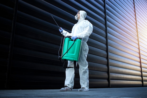 Person in white chemical protection suit doing disinfection and pest control and spraying poison to kill insects and rodents