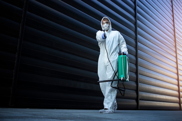 Person in white chemical protection suit doing disinfection and pest control and spraying poison to kill insects and rodents