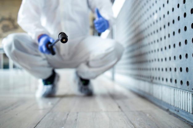 Person in white chemical protection suit doing disinfection of public areas to stop spreading highly contagious corona virus