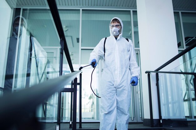 Person in white chemical protection suit doing disinfection of public areas to stop spreading highly contagious corona virus