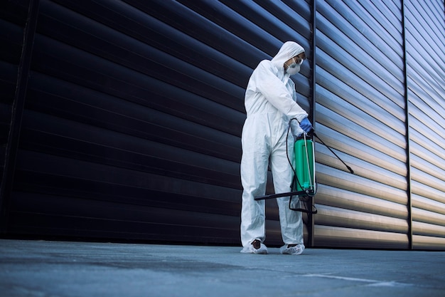 Free photo person in white chemical protection suit doing disinfection of public areas to stop spreading highly contagious corona virus