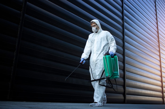 Человек в белом костюме химической защиты проводит дезинфекцию общественных мест, чтобы остановить распространение очень заразного вируса короны