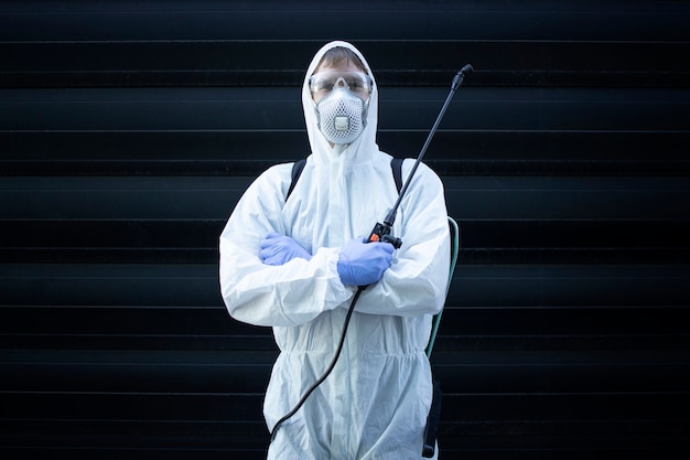 Person in white chemical protection suit holding sprayer with disinfectant chemicals to stop spreading highly contagious virus