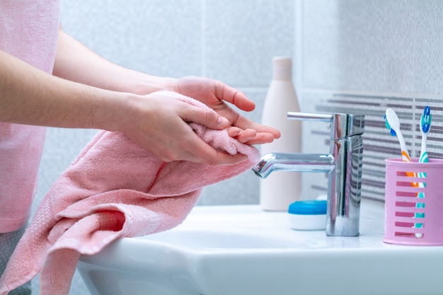 Person wipe hands dry with towel after washing in bathroom at home. hygiene and hand care.
