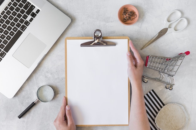 Free photo person with clipboard near laptop, shopping trolley and magnifier