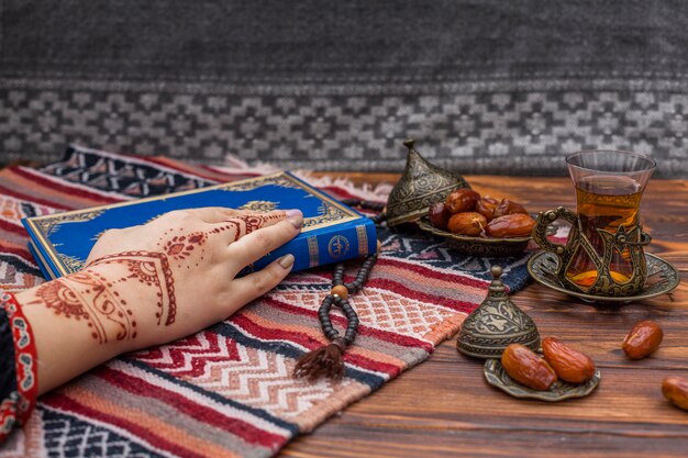 Person with mehndi holding Quran book near tea 