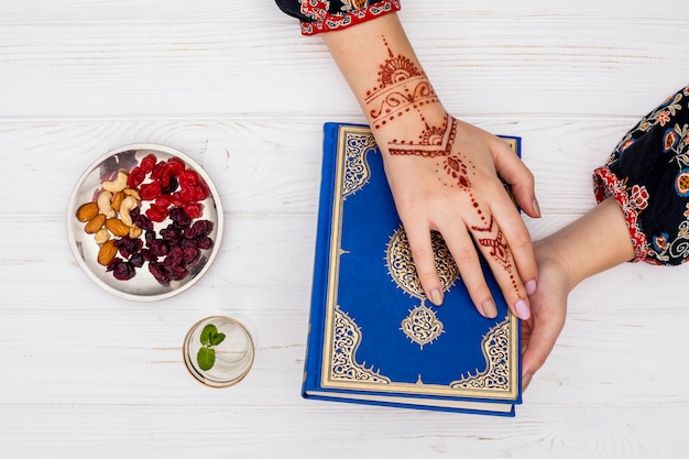 Foto gratuita persona con mehndi in possesso di corano vicino frutta secca