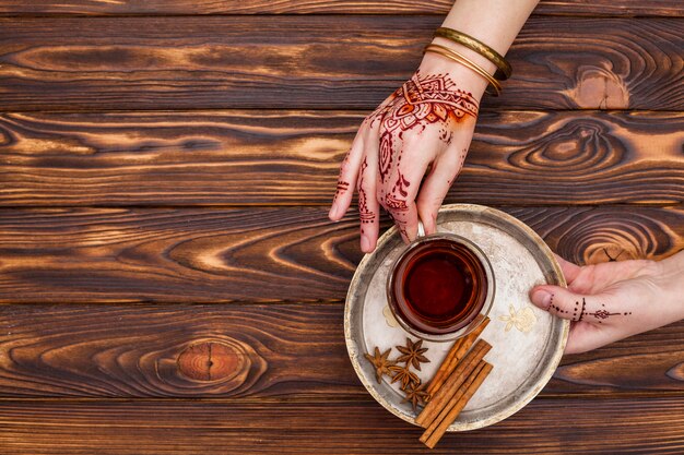 Person with mehndi holding tea cup on big plate 