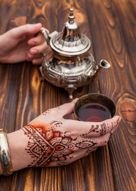 Person with mehndi holding teapot and cup