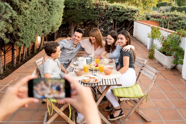一緒に屋外で昼食をとっている家族の写真を撮るスマートフォンを持つ人