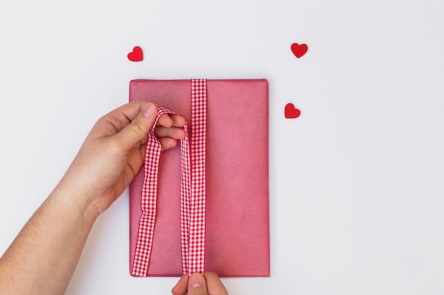 Person wrapping pink gift box on white table