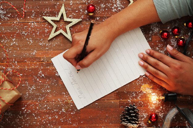 Person writing letter on wooden table with Christmas decoration