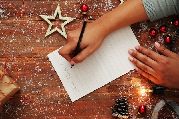 Person writing letter on wooden table with Christmas decoration