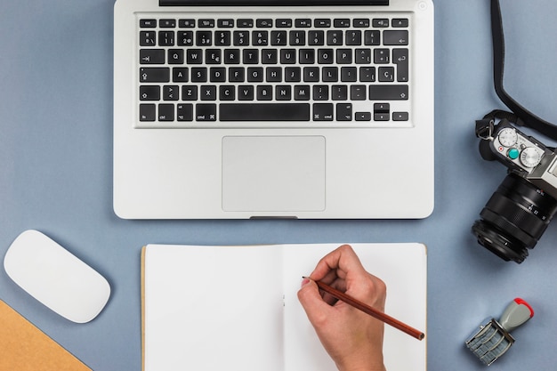 Free photo person writing on notebook at table with laptop