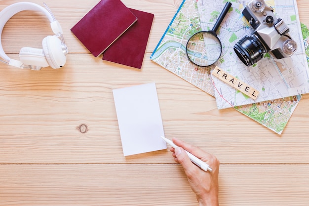 A person writing on paper with traveler accessories on wooden background