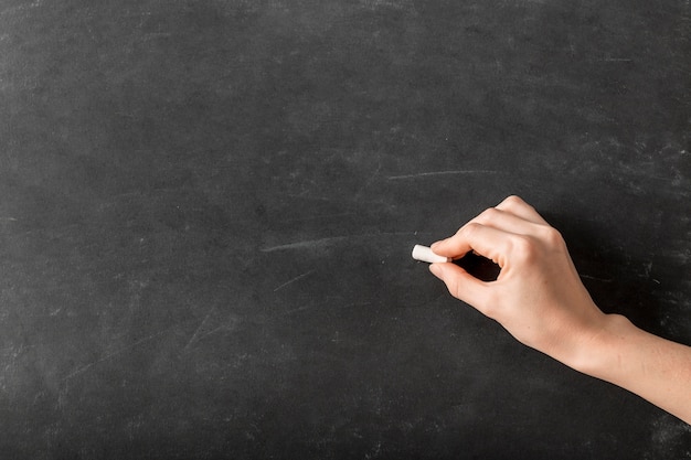 Person writing with chalk on an empty blackboard