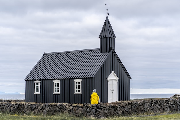 Человек в желтом пальто сидит на маленькой стене перед Бууаром в Исландии