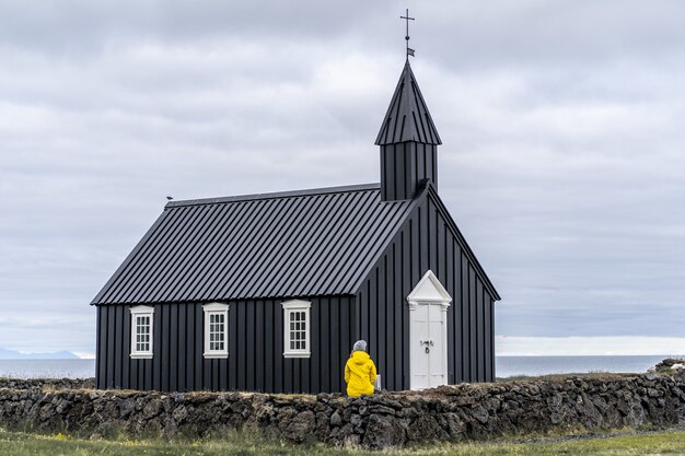 アイスランドのブオワールの前の小さな壁に座っている黄色いコートを着た人