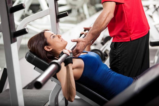 Personal trainer helping a young woman lift a barbell while working out in a gym