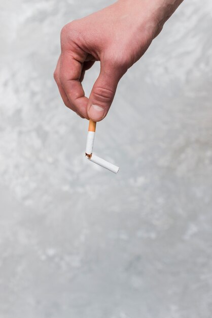 a persons hand holding broken cigarette on old wall background