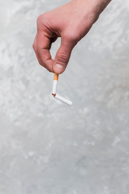 A persons hand holding broken cigarette on old wall background