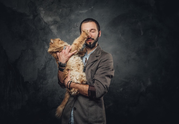 Pet owner in blazer is holding big and fluffy cat at dark photo studio.