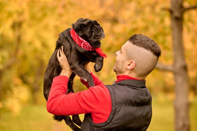 A pet owner with his friend. A man standing in the park and holding his cute dog