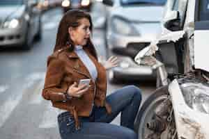 Free photo petrified woman feeling shocked while looking at her damaged car after the accident