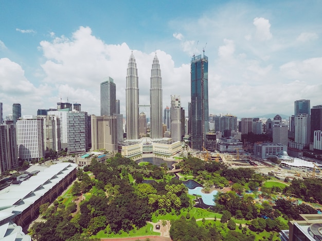Petronas Twin Towers near skyscrapers and trees under a blue sky in Kuala Lumpur, Malaysia