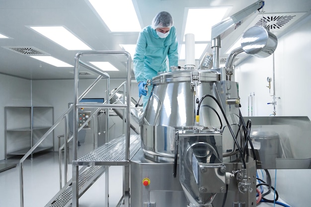 防護服の製薬工場の男性労働者は、滅菌作業条件で生産ラインを操作します。