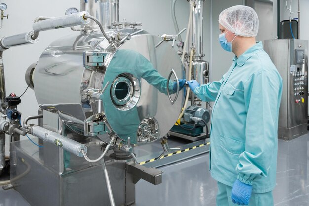無菌作業条件で機器に取り組んでいる防護服の製薬工場の男性労働者
