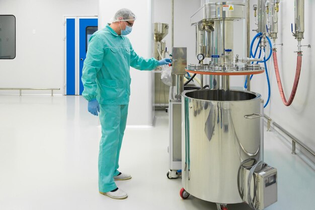 Pharmaceutical factory man worker in protective clothing working with control panel in sterile working conditions