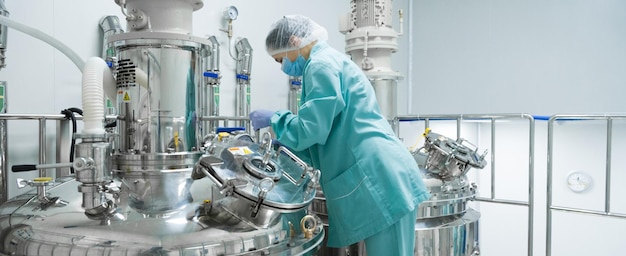 Pharmaceutical factory woman worker in protective clothing operating production line in sterile environment