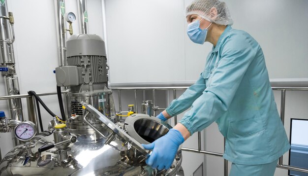 Pharmaceutical factory woman worker in protective clothing operating production line in sterile environment