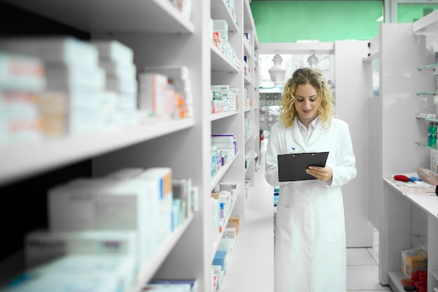 Foto gratuita farmacista in uniforme bianca che cammina dallo scaffale con i medicinali e controlla l'inventario